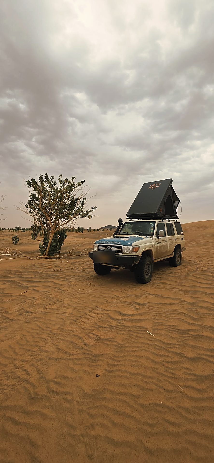 LCM hardshell rooftop tent open on a dune under a cloudy sky