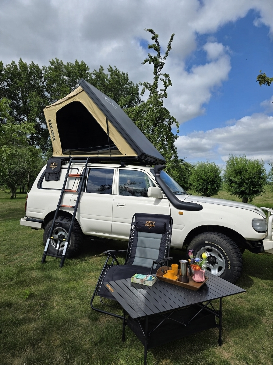 LCM Offroad Savannah hardshell rooftop tent in khaki, open on a white Toyota Land Cruiser with camping chair and aluminium table in a meadow