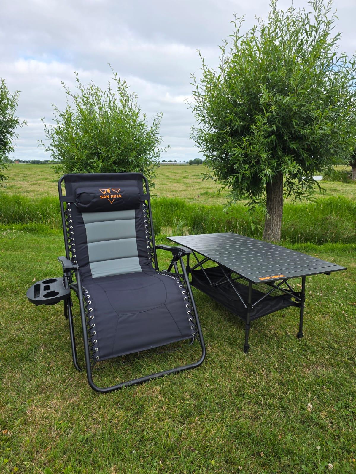 SAN HIMA luxe campingstoel met bekerhouder naast aluminium campingtafel in het weiland