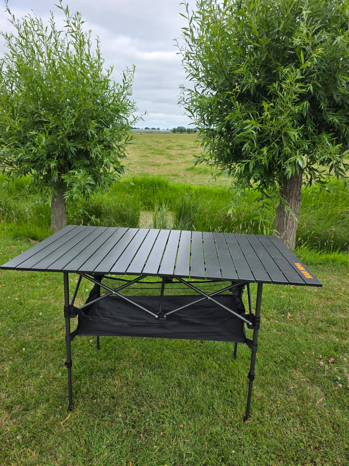 Aluminium campingtafel SAN HIMA met lattenblad en opbergnet eronder in het weiland