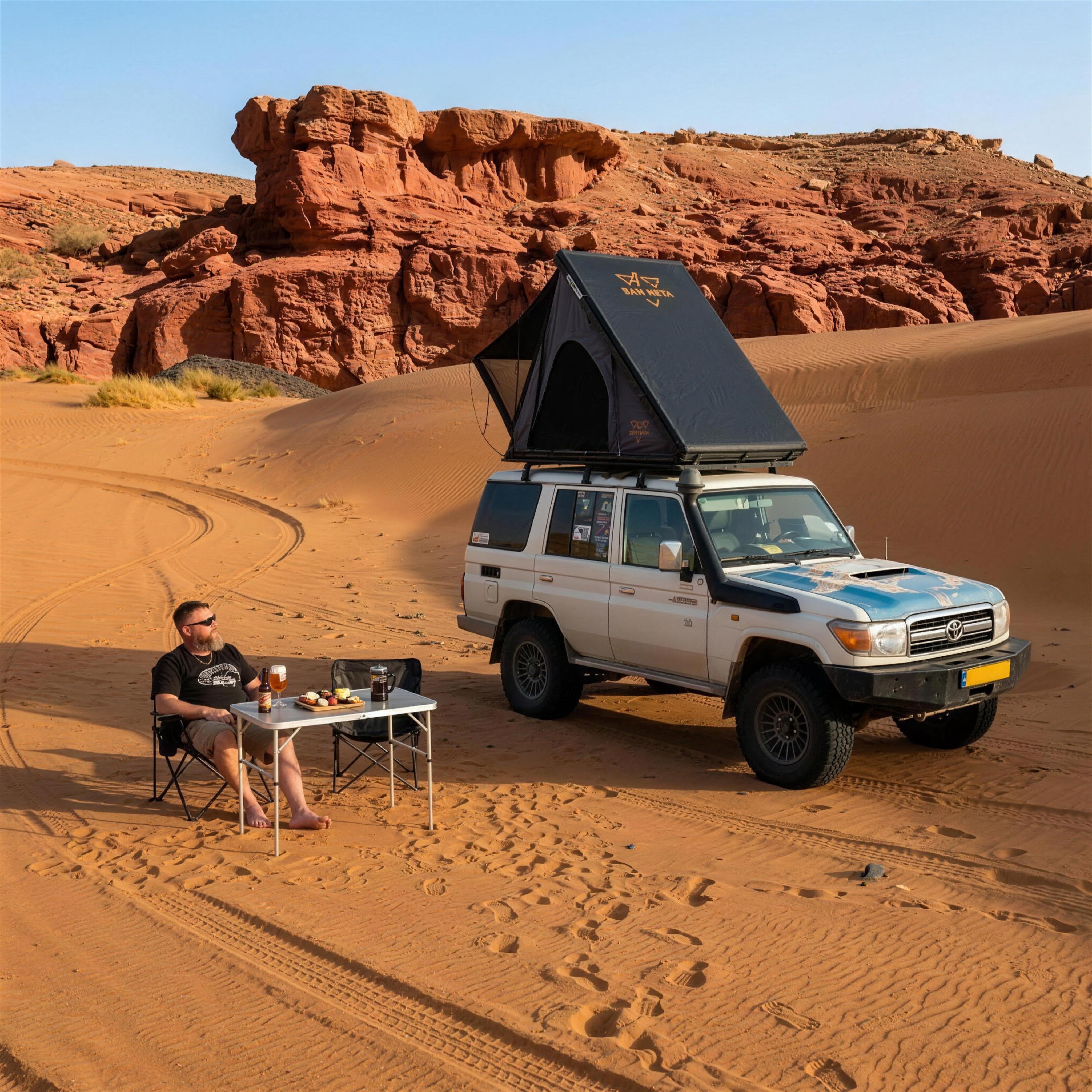 Kampeerder aan een campingtafel naast een 4x4 met opengeklapte LCM Offroad Dune hardshell daktent in de woestijn